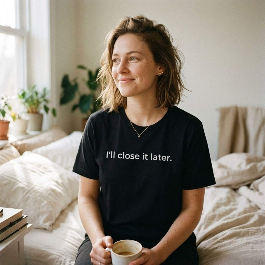 woman in i'll close it later dark ash tee holding coffee on bed — text & tone