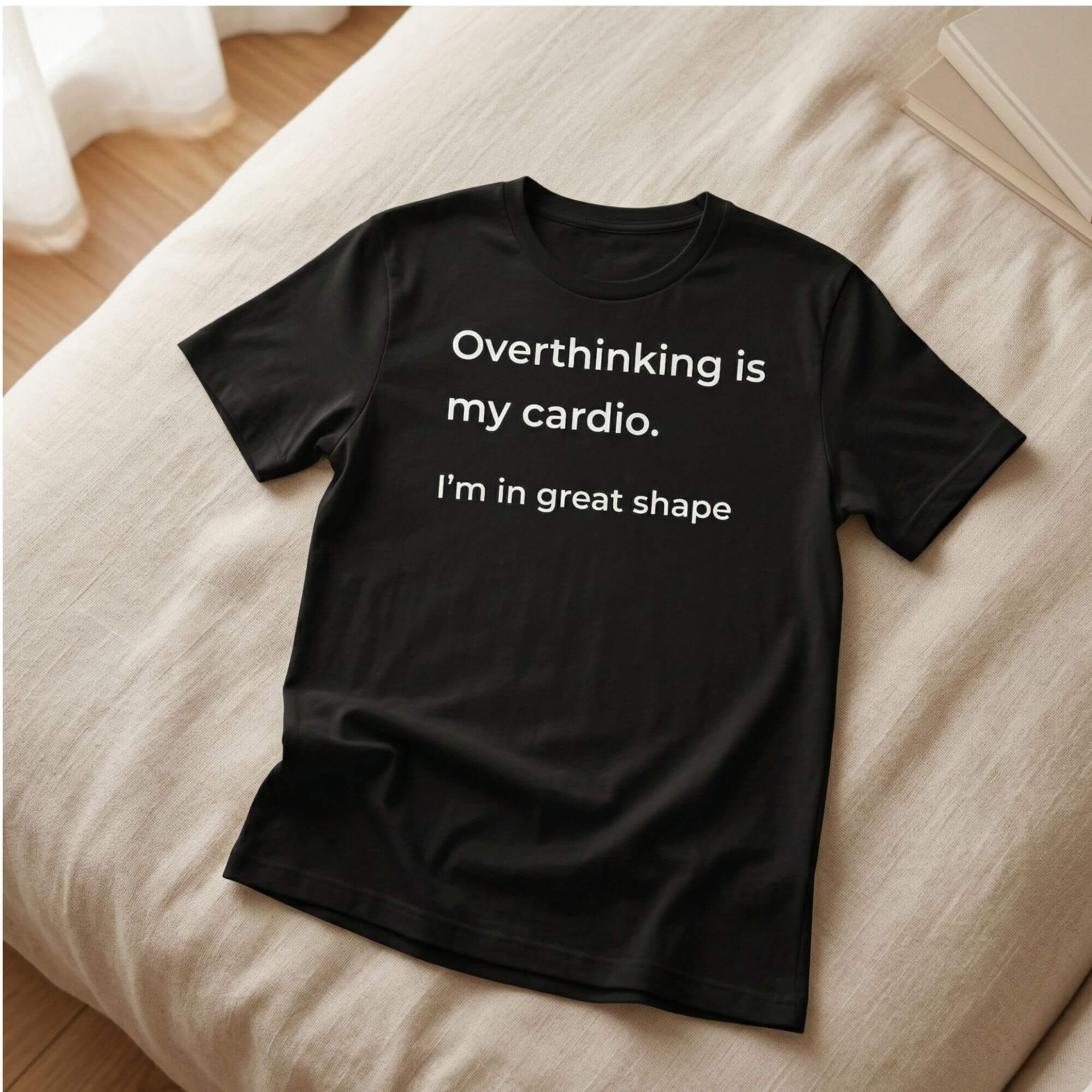 Black t-shirt with "Overthinking is my cardio. I’m in great shape" text on a neutral bed background
