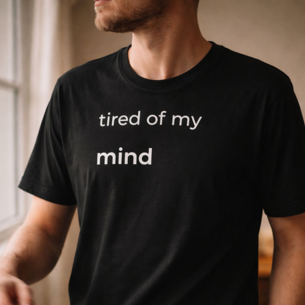Person wearing black t-shirt with small text “tired of my mind”, close-up chest view, soft natural lighting, minimal style