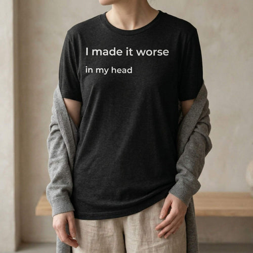 Person wearing black slogan t-shirt with “I made it worse in my head” in a minimal indoor setting