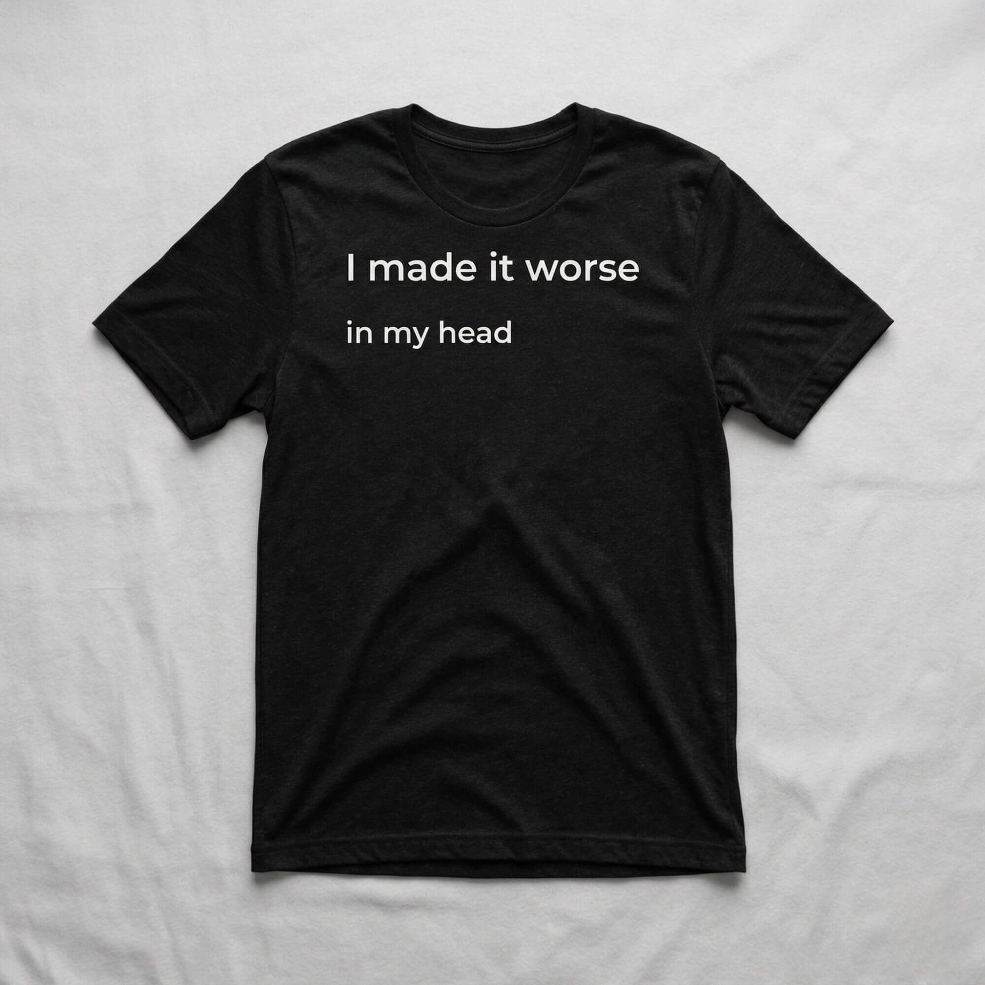 Black graphic t-shirt with “I made it worse in my head” text laid flat on soft neutral fabric