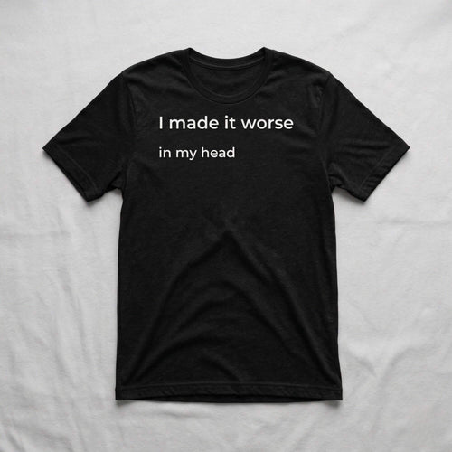 Black graphic t-shirt with “I made it worse in my head” text laid flat on soft neutral fabric