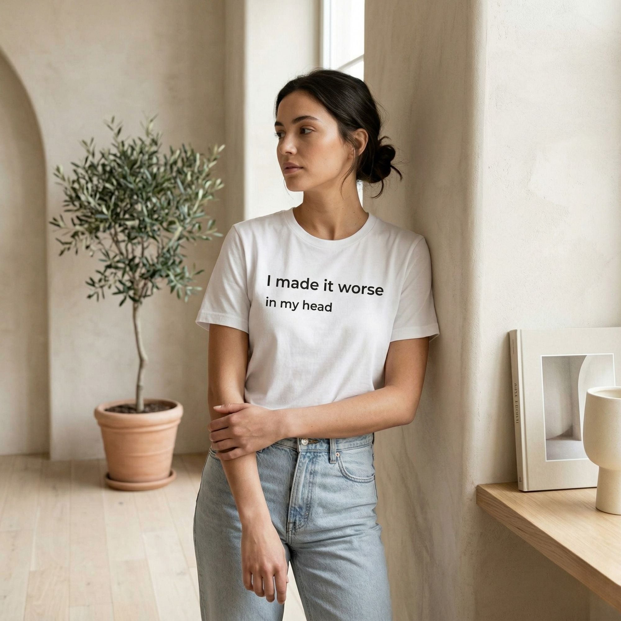 Woman wearing a white t-shirt with text, standing in a room with a plant and framed picture.