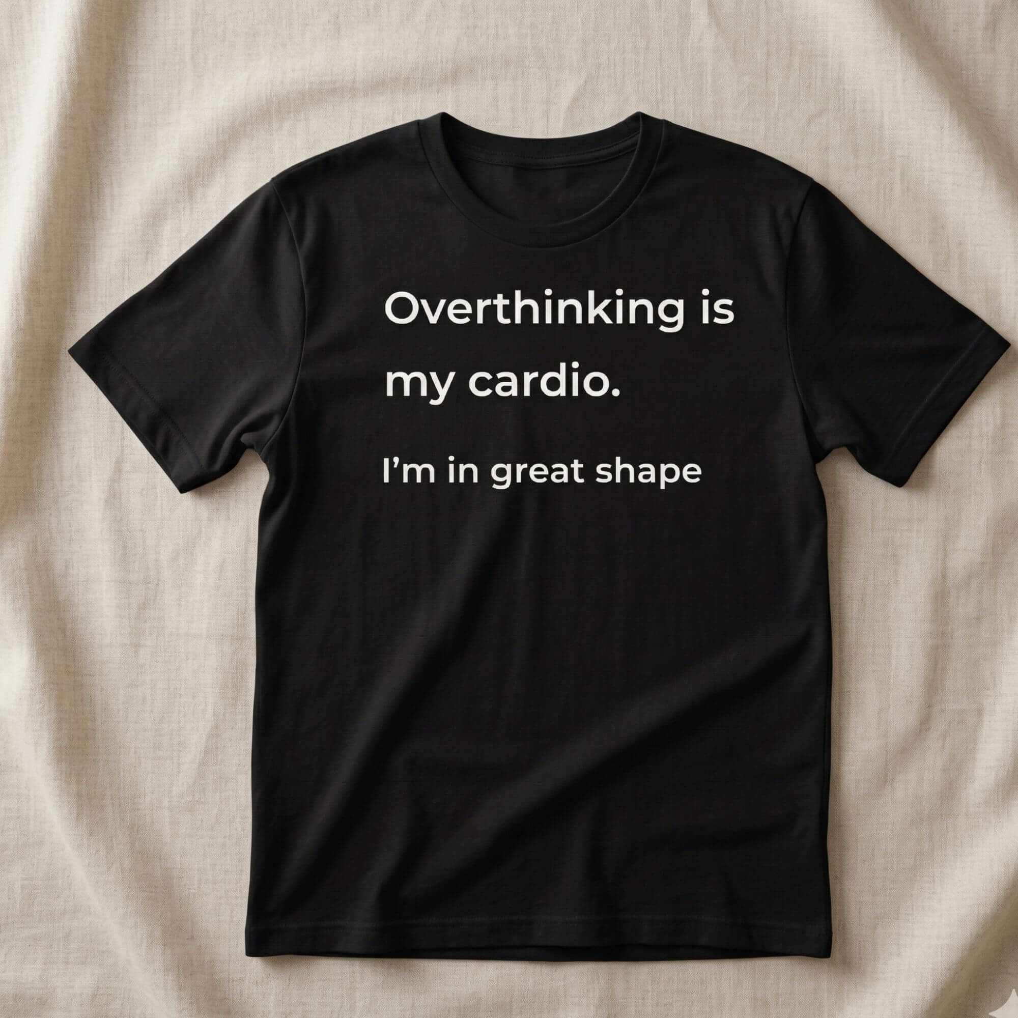 Black t-shirt with white text "Overthinking is my cardio. I’m in great shape" flat lay on neutral fabric